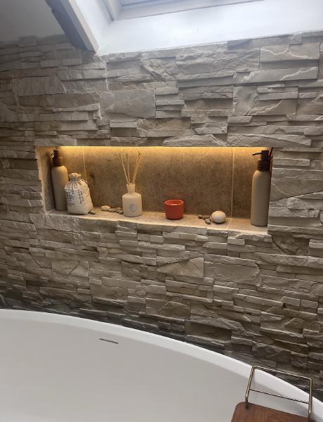 Warm LED strip lighting in a stone-clad bathroom alcove beside a freestanding bath